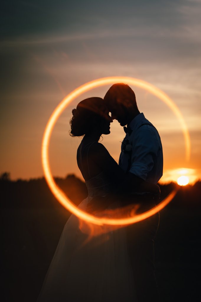 Silhouette of bride and groom in front of the setting sun and a ring of fire around them 