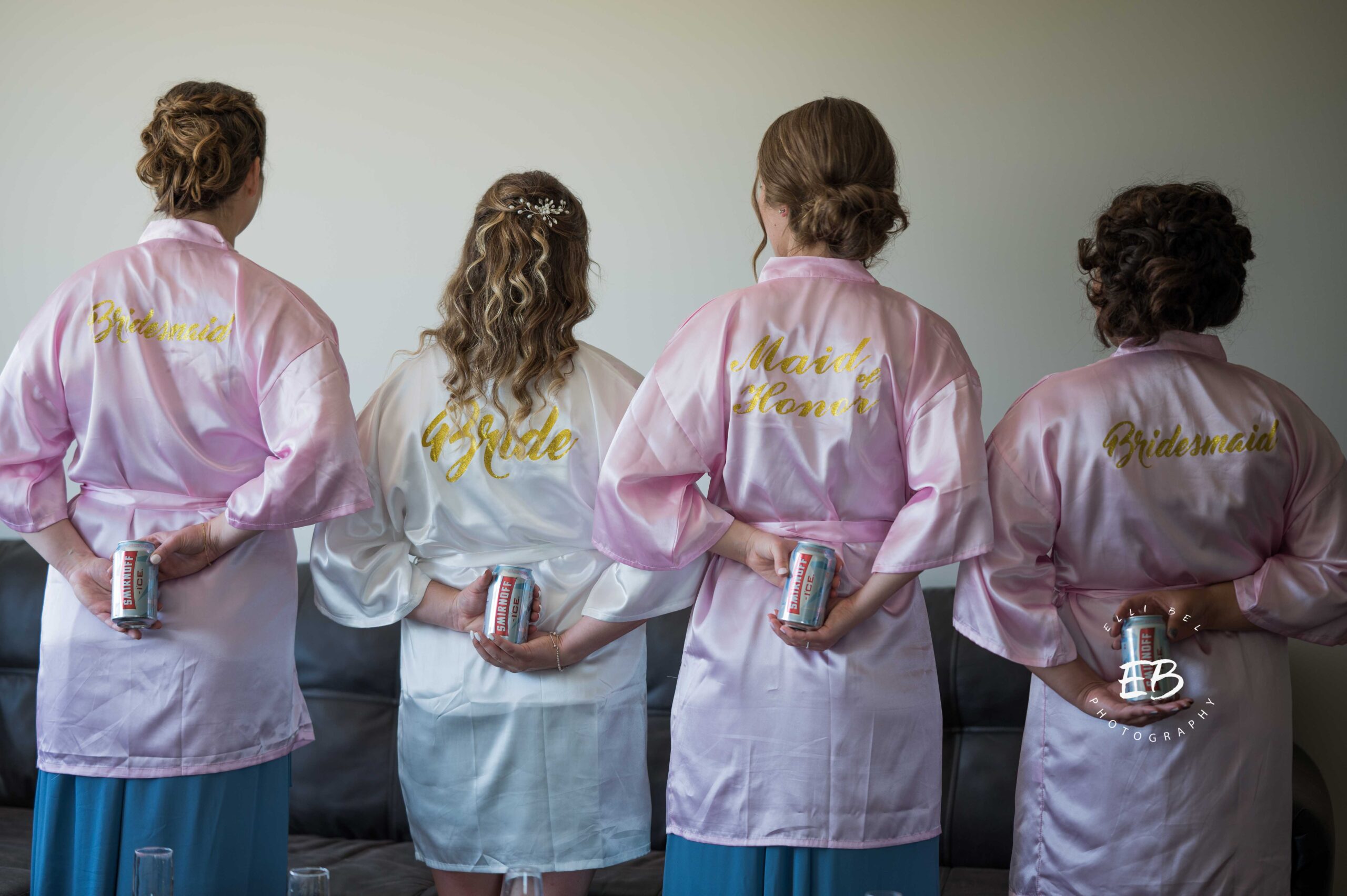 bridesmaids and bride holding beer cans behind their backs, facing away from camera
