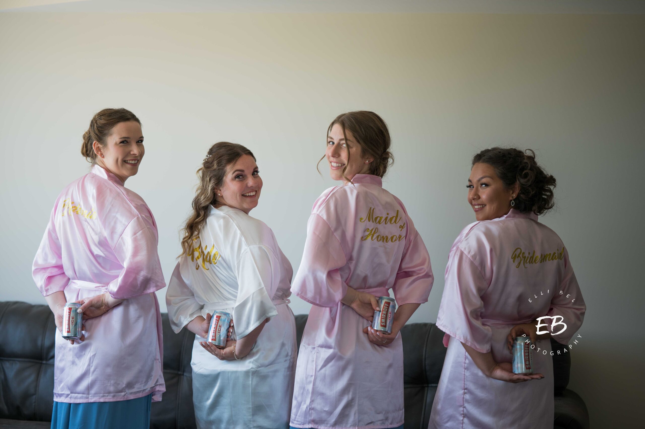 bridesmaids and bride holding beer cans behind their backs, facing the camera