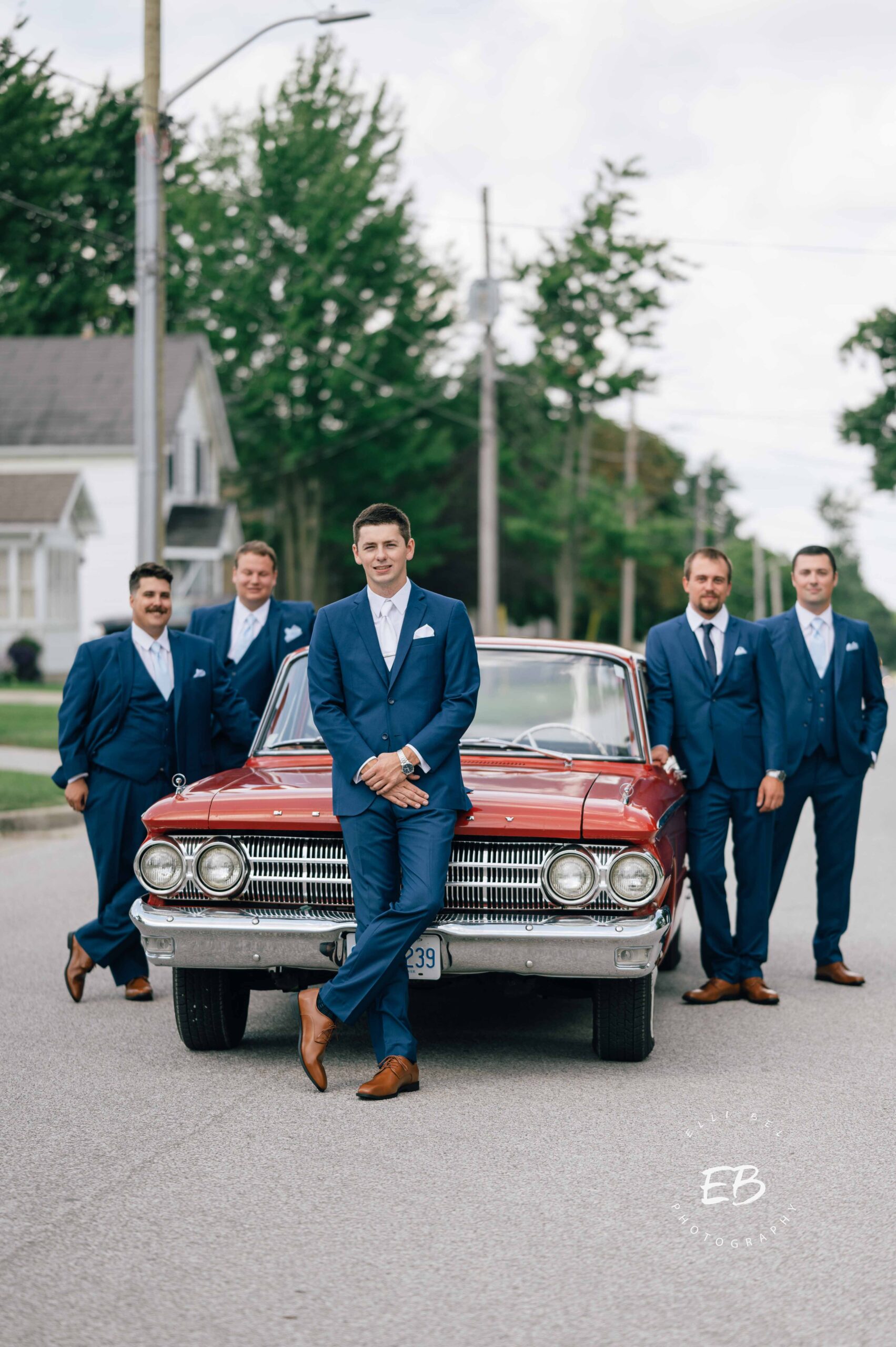 groom  and groomsmen in front of a red sports car